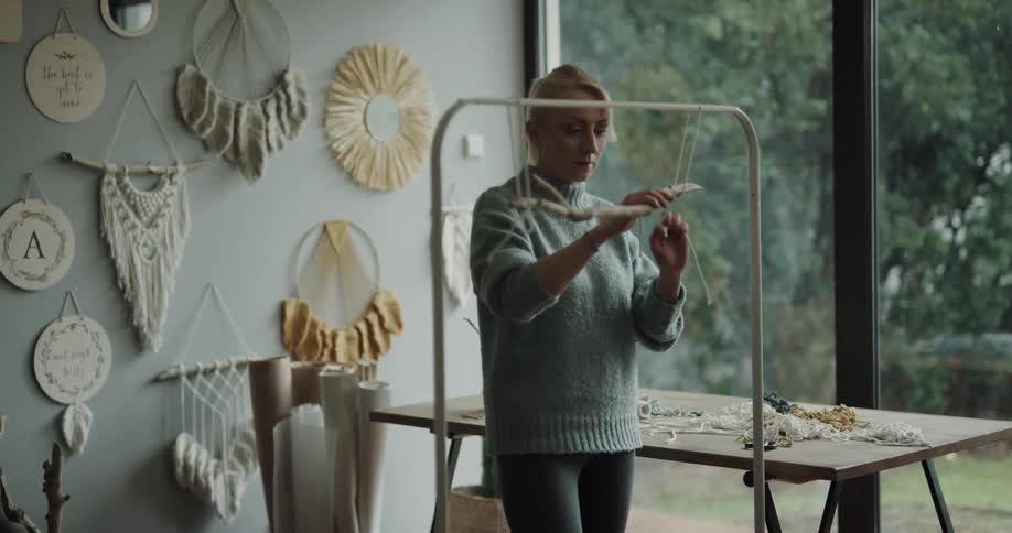 Woman crafting decorations using strings and sticks inside a studio