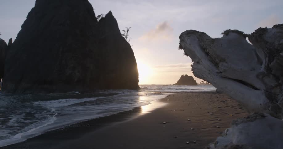 The sun is setting behind a large rock in the beach