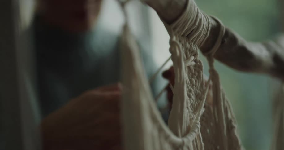 A woman knitting on a stick hanging in the air