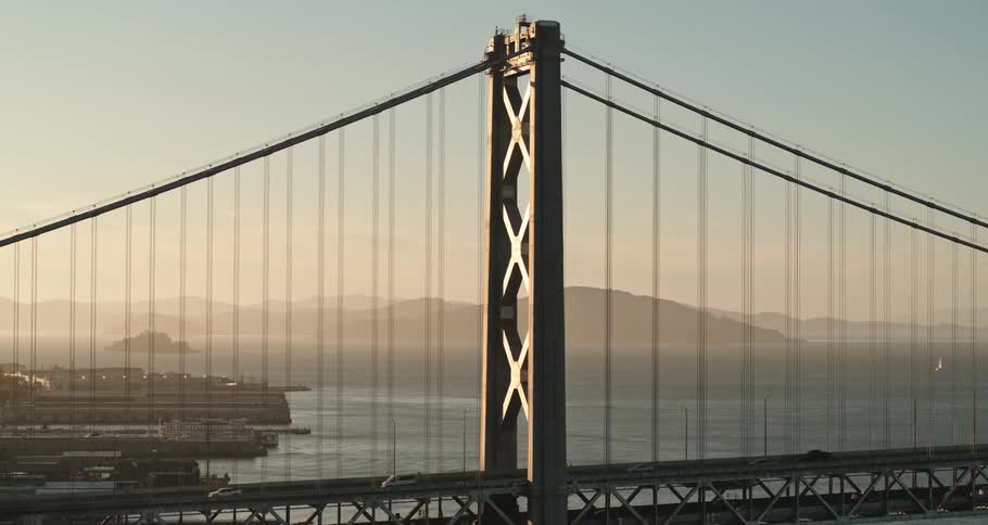 Traffic crosses suspension bridge toward city as fog obscures mountains across water