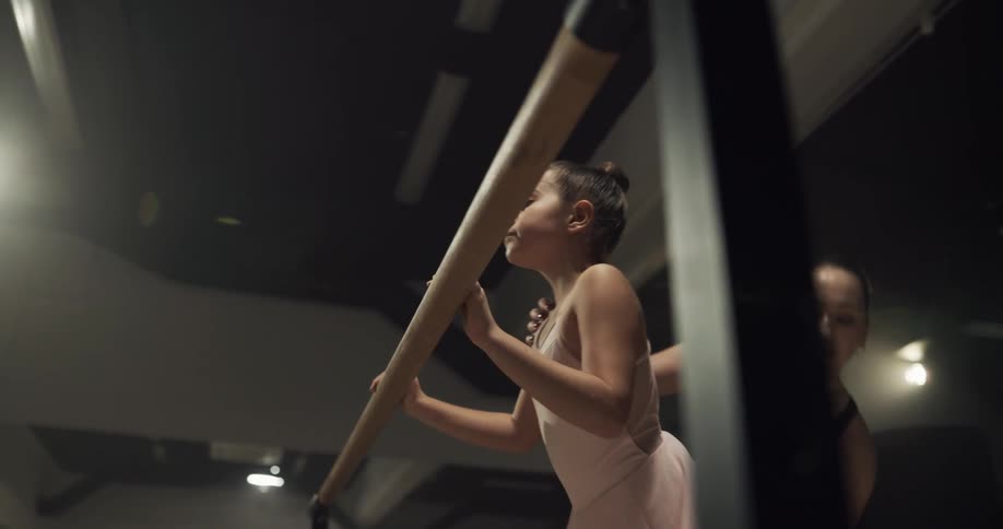Ballet instructor teaching a young girl stretching her leg in a studio