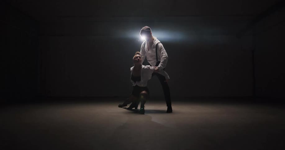 A man and woman salsa dancing in front of a spotlight