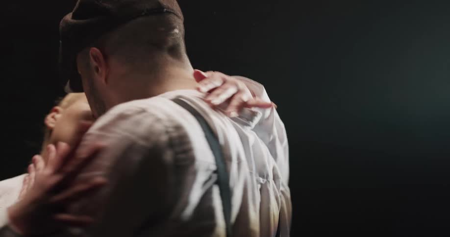 A man and woman dance and touch in a sexy manner under a spotlight
