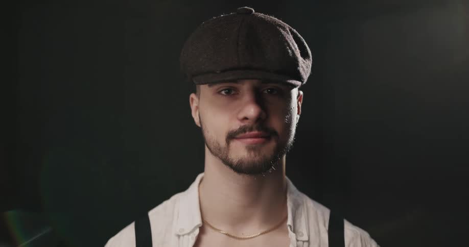 Man with white shirt black cap and beard faces the camera with eye contact