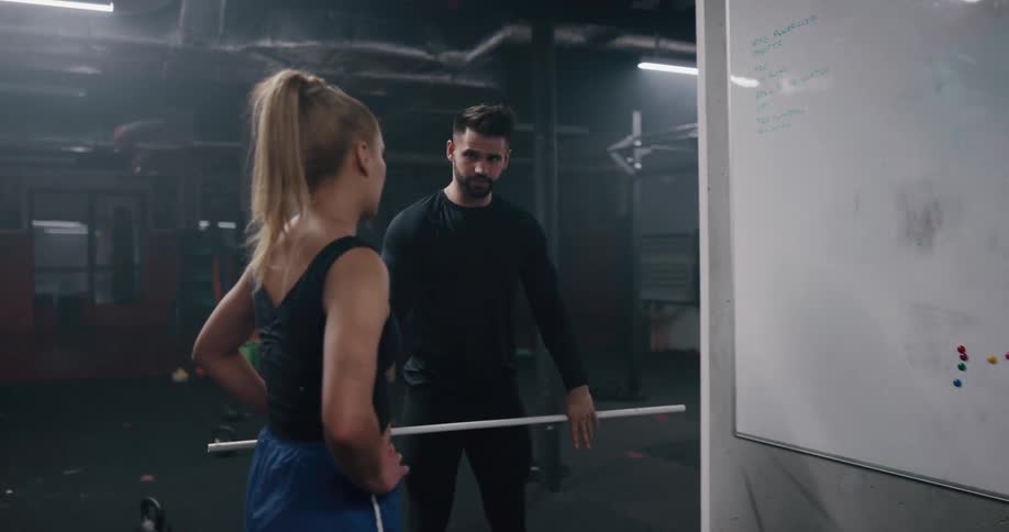 A coach points at a whiteboard and demonstrates an exercise to a teenage girl