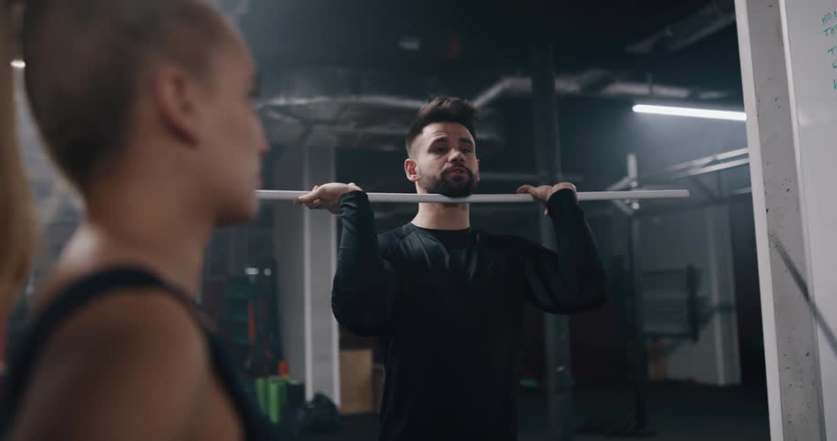 A man talks with a woman while lifting a bar