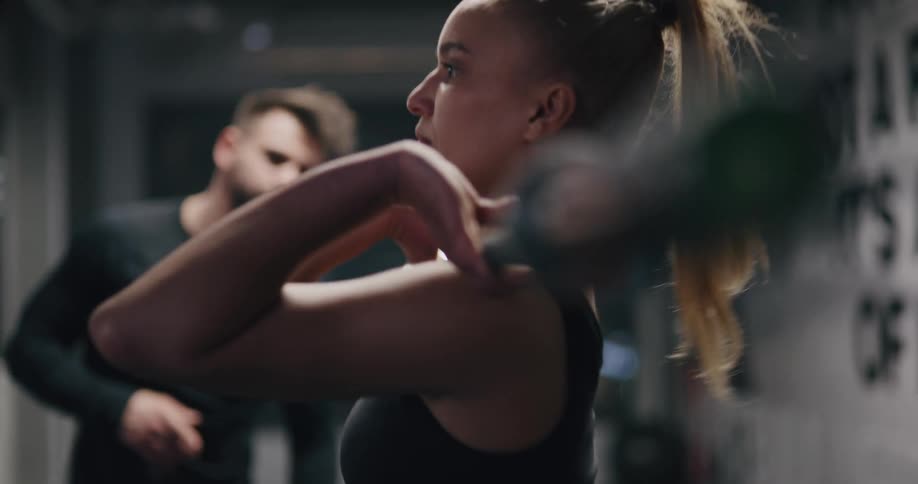 While being watch by a trainer a young women performs a quick weight lifting maneuver with a heavy olympic bar