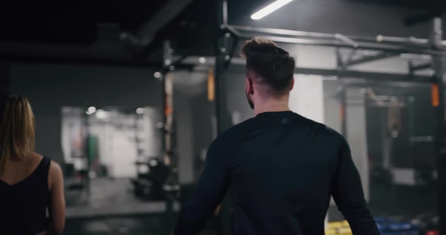 A man and woman standing in a gym at night high five one another before walking towards the exit