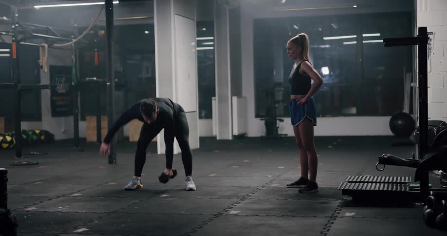 Personal trainer teaching a student exercises with dumbbells inside a gym