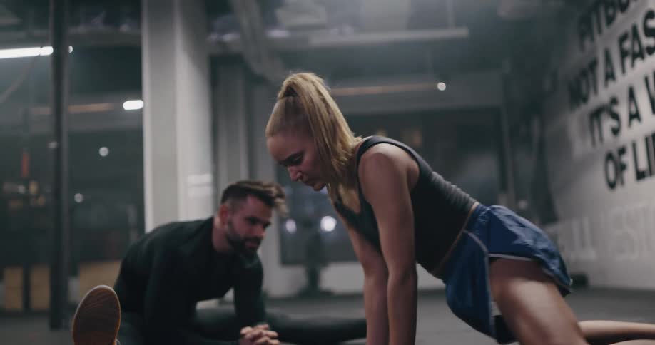 A woman does stretches on the floor of a gym at night next to a man who is also stretching