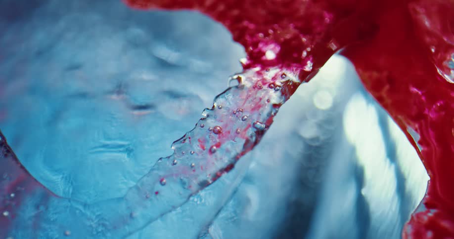 Bright red liquid ink flowing on the cracked jagged surface of clear blue ice