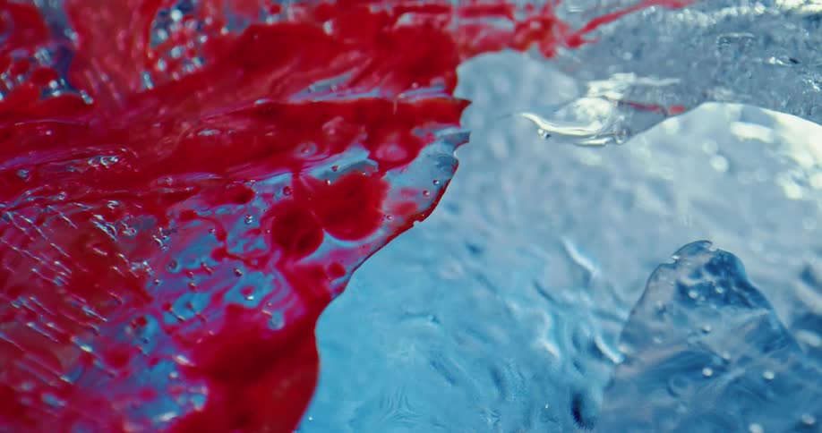 Bright red liquid ink spilling on the cracked surface of blue clear ice