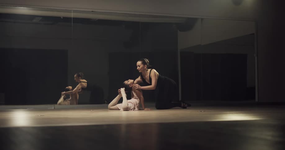 A young ballerina practices ballet poses as her instructor gives her guidance
