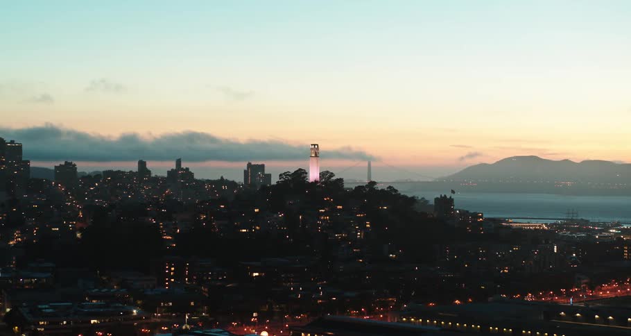 An aerial view of a lit up city skyline with the coast and water in the distance