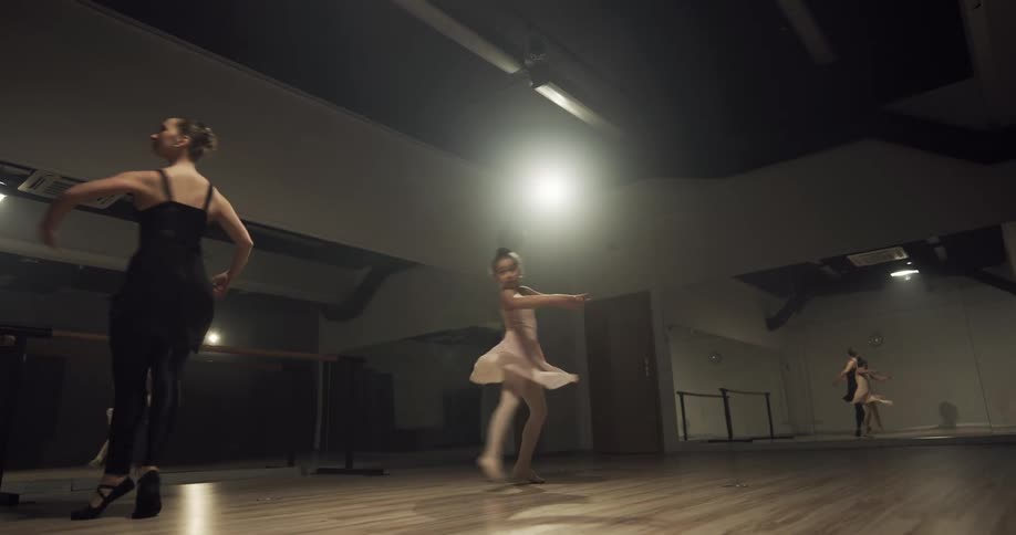 Woman teaching girl ballet in front of full wall mirrors in a dance studio