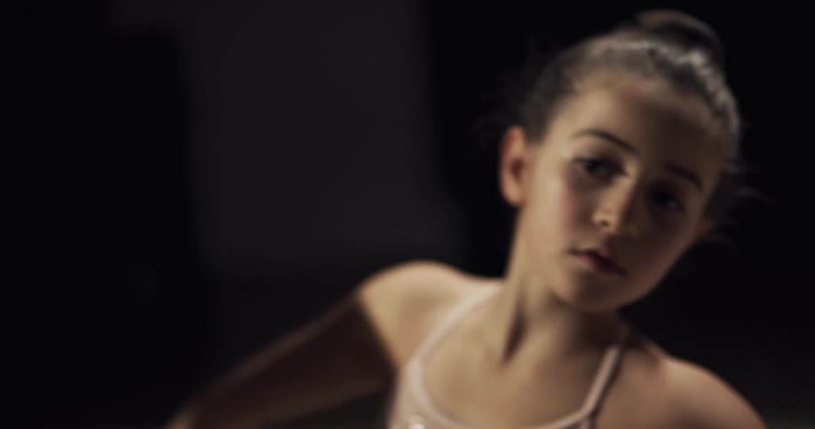 A young ballet dancer follows along with her teacher as they practice in front of mirrors