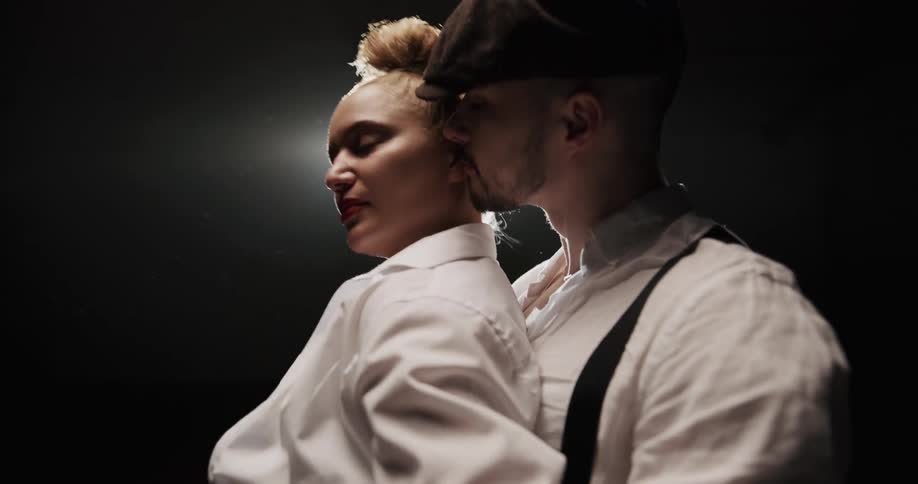 A woman walks up to her dance partner and touches his neck as they start doing the tango