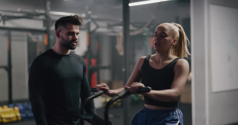 A trainer encourages a woman working out on a bike in a gym