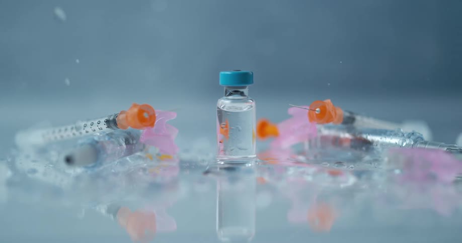 Syringes and medicine bottles over a reflective surface with water splashing