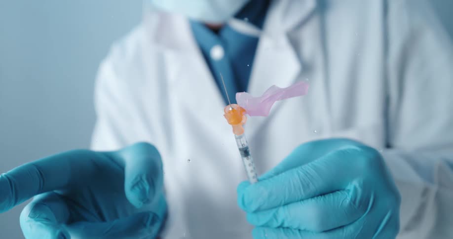 A doctor flicking the tip of a needle shaking liquid droplets