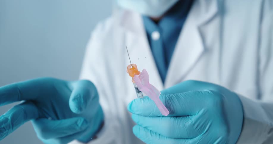 A doctor with a mask and gloves flicking a syringe