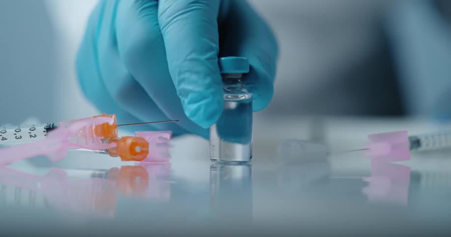 A medical professional holds onto a small glass vial of a clear liquid