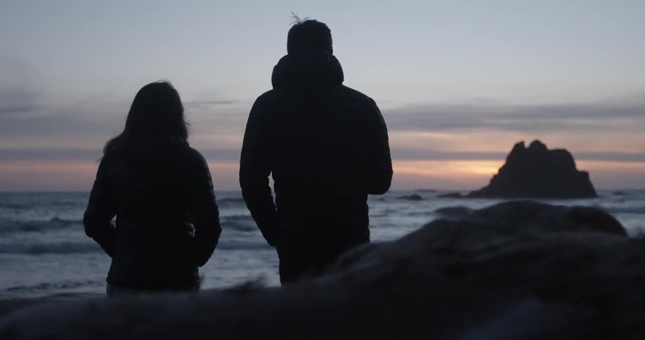 A man and woman chat on a beach at sunset