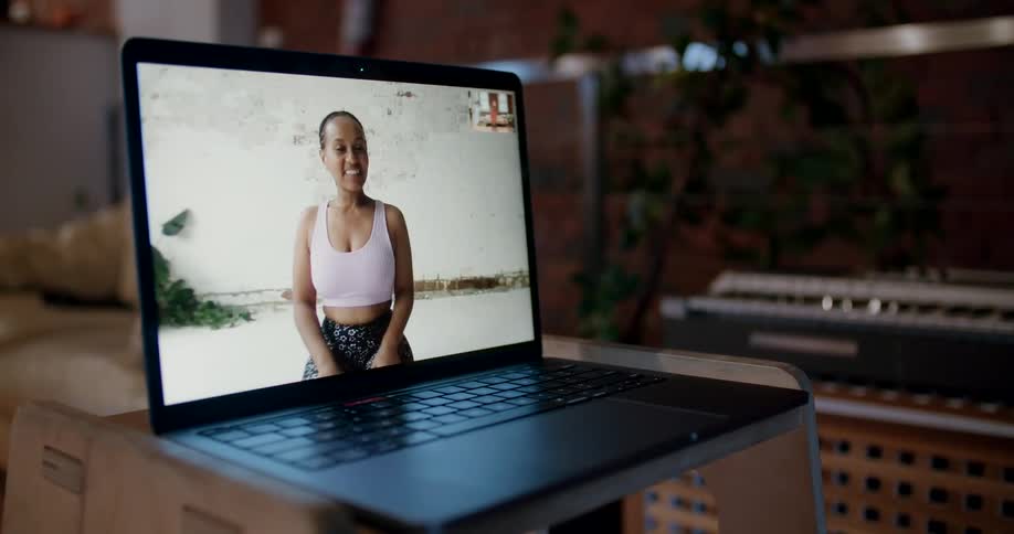 A woman in a sports bra waving and smiling from a computer screen
