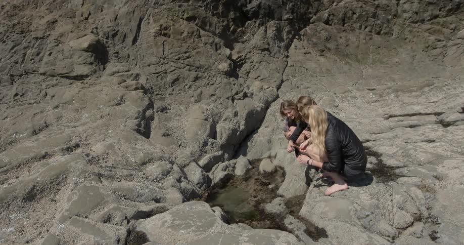 Three people are crouched by a hole in rocks