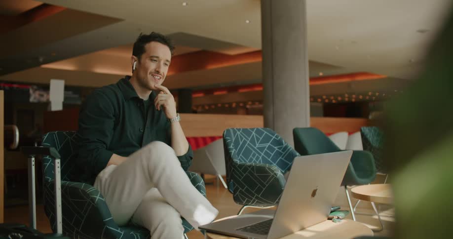 A man sits back in his chair as he continues to talk and smile during a video call on his laptop