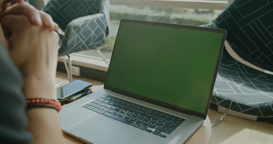 A person staring at a laptop with a green screen