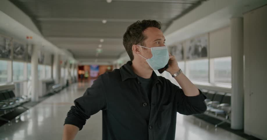 A man stands in an airport terminal talking on a cell phone and looking around confused