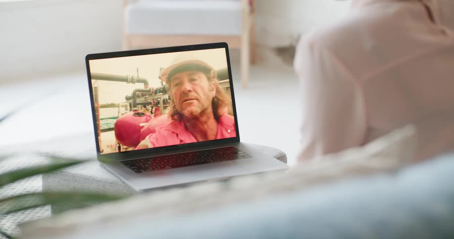 A woman in a room sitting on a couch video chatting on a laptop with a chair in the background