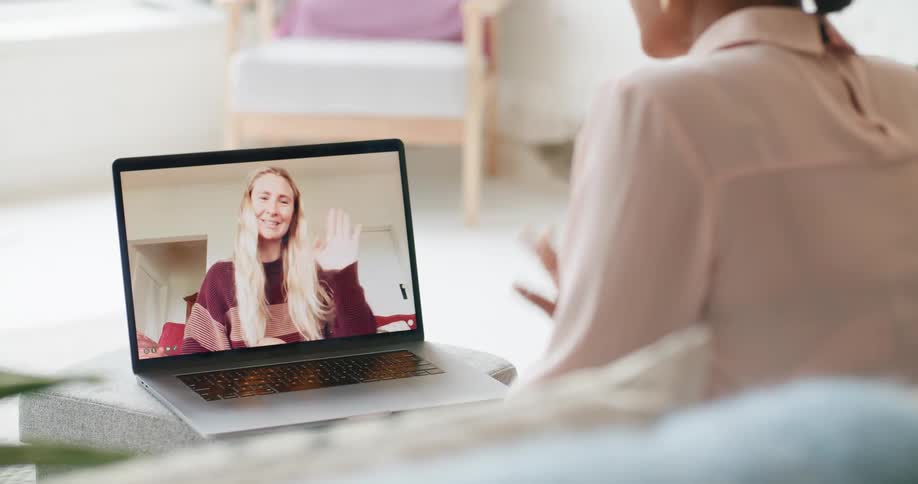 A woman on a laptop screen waves good bye to a woman sitting on a couch as they video chat