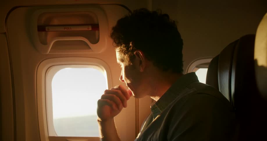 A man sits in an airplane seat and types on a laptop on his lap