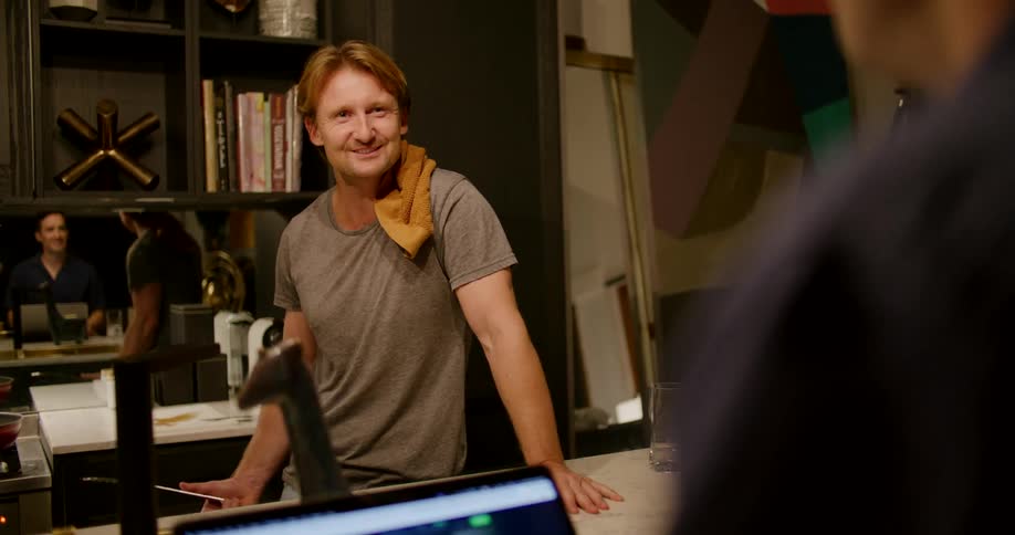 Two men talking at a table in a shop and laughing