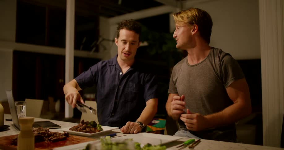 Two men chatting while eating dinner at a counter