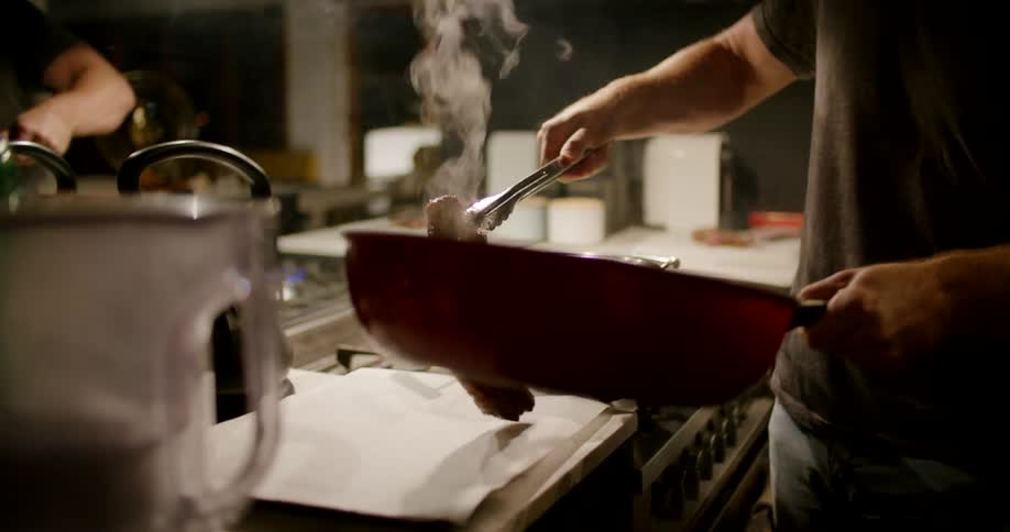 A man cooking a steak in a pan in a kitchen