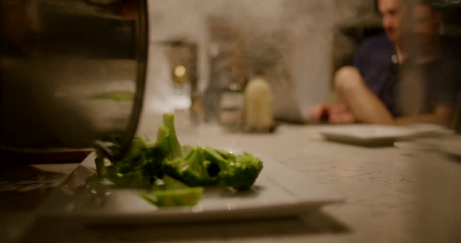 A man dumping steamed broccoli onto a plate