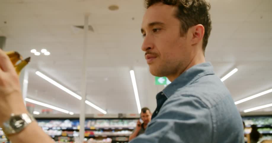 A man inspects a small bunch of bananas at a grocery store before putting them in his basket