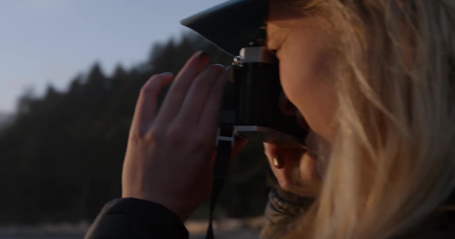 A person is taking photographs near the water at sunset