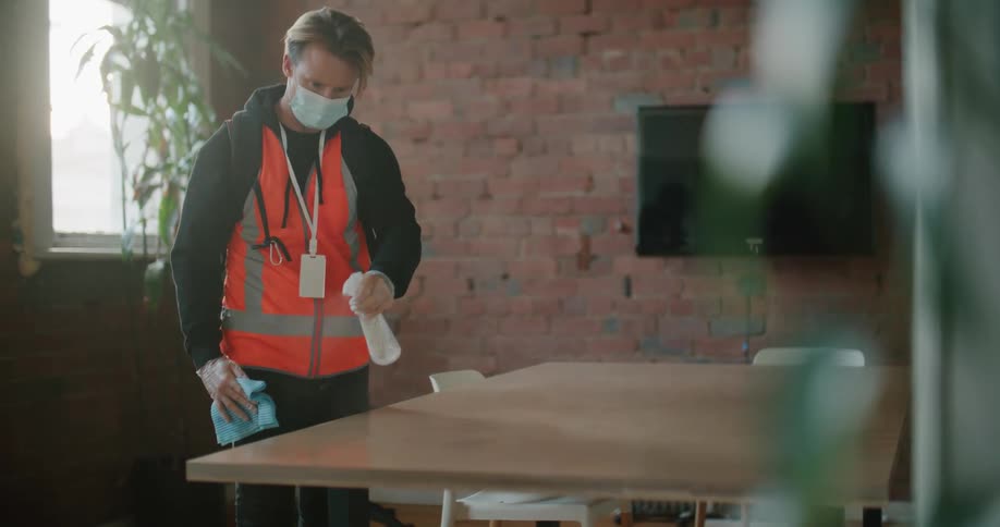An employee spraying and wiping down a table in an office