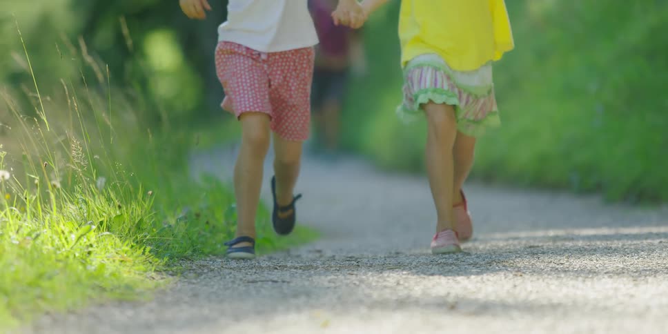 Two young girls hold hands and skip along a gravel path