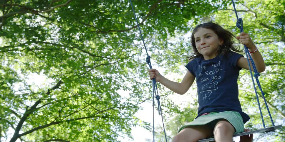 A young girl swings on on an outdoor swing with mountains in the distance
