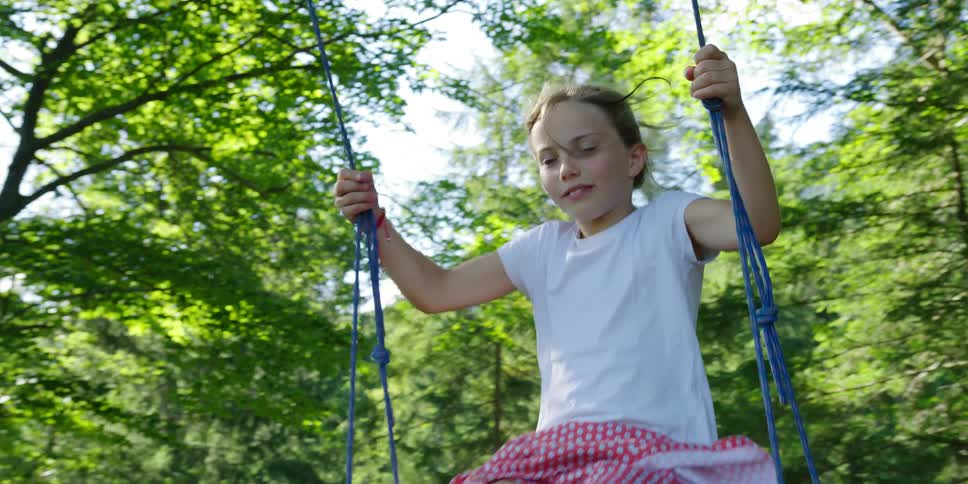 A girl smiles as she holds on tight to a swing attached to a tree in a forest