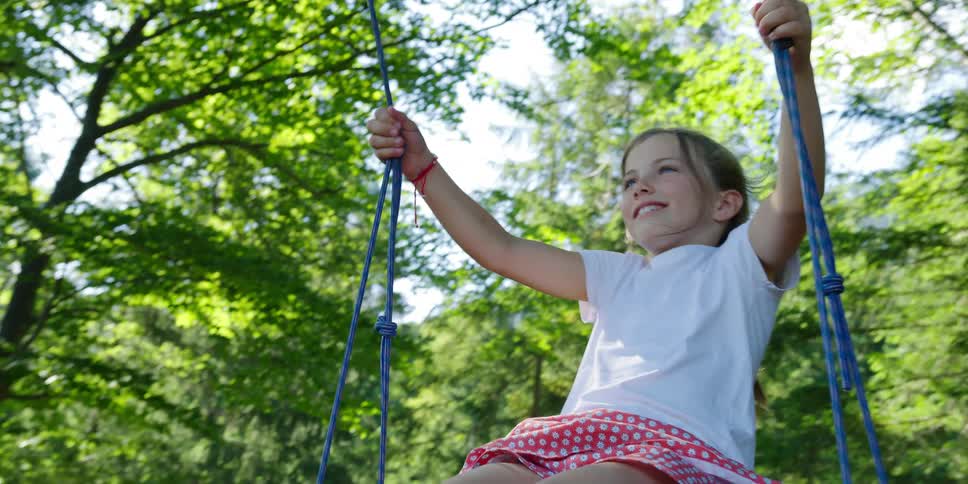 A smiling girls swings on a tree swing in a woodland on a sunny day
