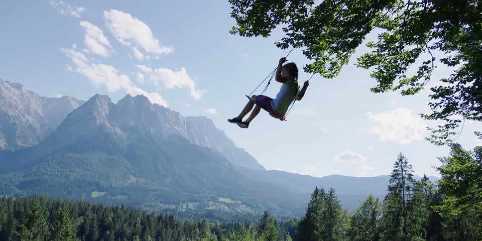 A girl swinging on a swing above a forest