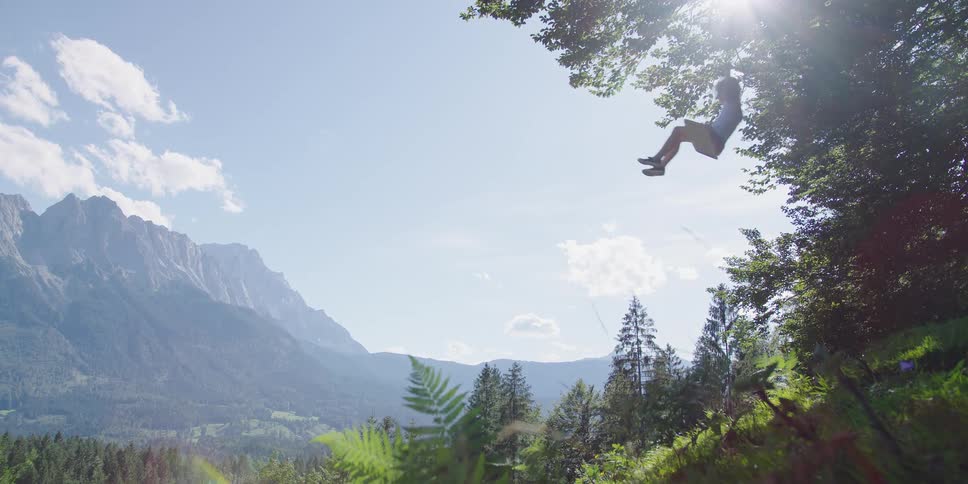 A child swings on swing set on the side of a hill in the countryside on a sunny day