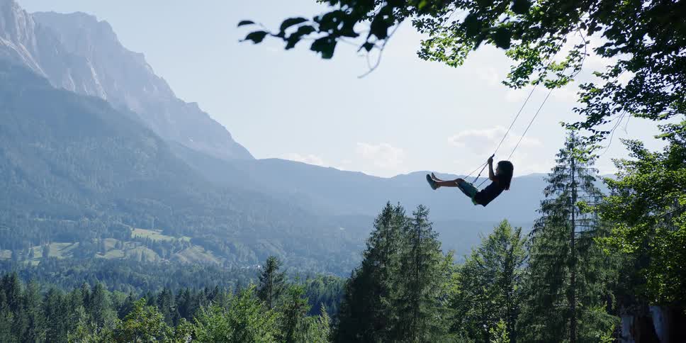 A child swinging in front of a hilly forest