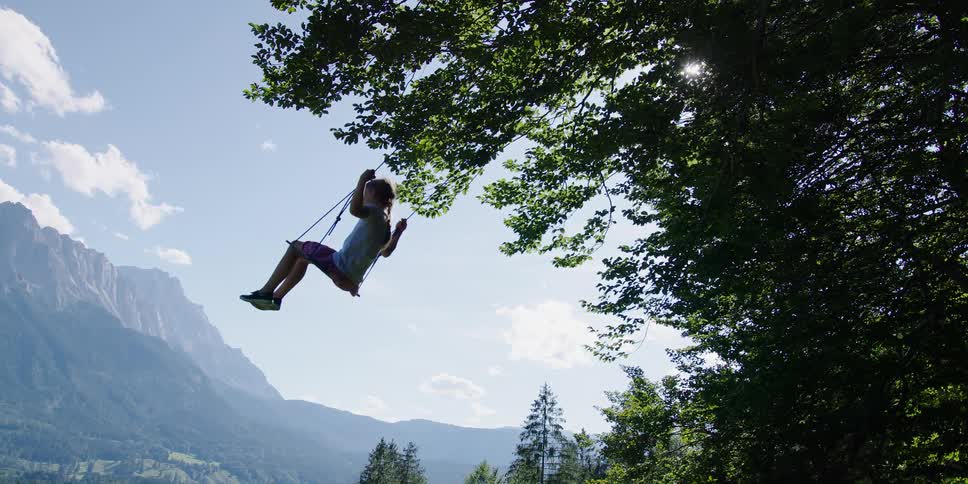 A girl swinging on a swing with trees a mountain range the sky and clouds in the background